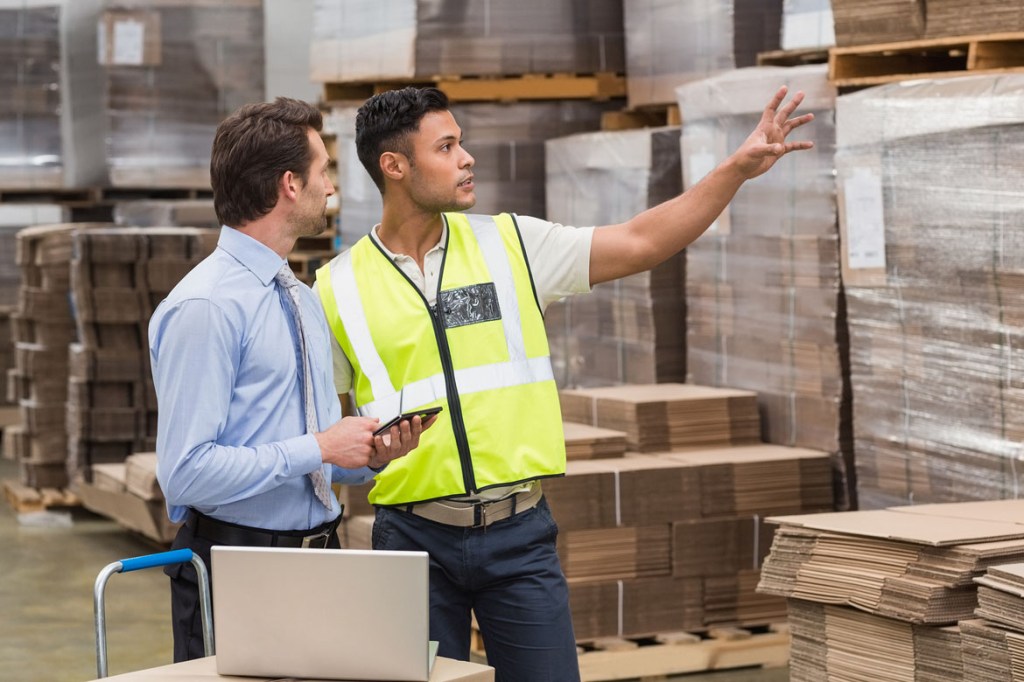Warehouse worker showing something to his manager in a large warehouse.